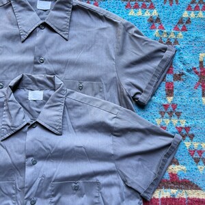 以下が含まれることがあります： 胸にポケットが付いたグレーの半袖ボタンダウンシャツが2枚です。