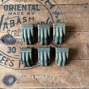 May include: Six antique brass furniture feet with a claw design. The feet are arranged in two rows of three on a wooden surface.