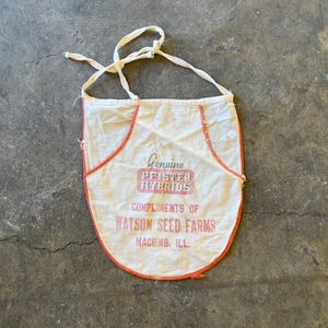 May include: White cotton apron with red trim and the text "Genuine Pfister Hybrids Compliments of Watson Seed Farms Macomb, Ill."