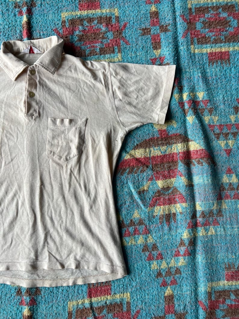 May include: A light beige short-sleeved polo shirt with a single button placket and a small pocket on the left chest.