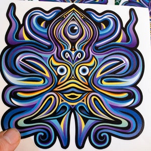 Puede incluir: Una pegatina colorida con un diseño psicodélico que presenta una cara con múltiples ojos y patrones en espiral en tonos de azul, morado, amarillo y negro.
