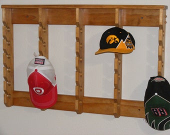 May include: A wooden hat rack with 12 slots for displaying baseball caps. Three hats are displayed on the rack, one red and white, one black and yellow, and one black and green with the number 88.