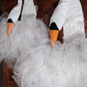Pu&ograve; includere: Due costumi da cigno bianchi con gonne di tulle e becchi arancioni. Le teste di cigno sono fatte di feltro e hanno occhi neri.