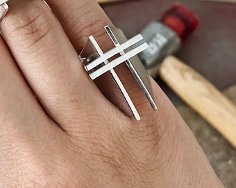 May include: Two silver rings with geometric designs. The rings are on a person's hand. The rings are both made of silver and have a simple, modern design.