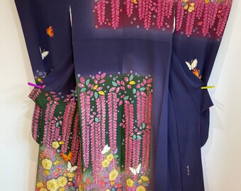 May include: A navy blue kimono with a floral and butterfly design. The kimono features a pattern of yellow flowers, pink wisteria, and colorful butterflies. The sleeves and hem are adorned with detailed artwork.