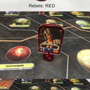 May include: A red plastic game piece with a clear plastic card featuring a picture of Wedge Antilles. The card has the text "WEDGE ANTILLES" and the number "3". The game piece is on a black and white game board with a red planet in the background.