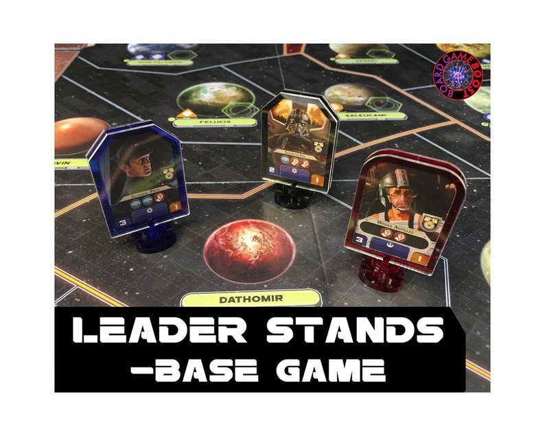 May include: Three clear plastic leader stands for the Star Wars: Rebellion board game. The stands are red, blue, and clear. Each stand has a character card with a picture of a character from the game. The text "Leader Stands - Base Game" is printed on the bottom of the image.