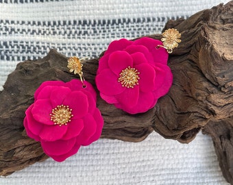 Pode incluir: Um par de brincos de flores cor-de-rosa com detalhes dourados. Os brincos são feitos de argila polimérica e têm um visual delicado e feminino.
