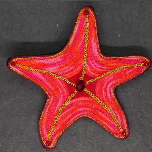 May include: A red and pink crocheted starfish with gold thread accents and red gem embellishments.