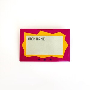 May include: A rectangular pin featuring a vibrant magenta border with a jagged orange inner frame surrounding a light gray center panel. The text "NICK NAME" is printed in a dark gray pixelated font on the upper left side of the gray panel.