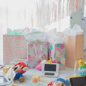 Puede incluir: Una mesa de fiesta con bolsas de regalo con patrones florales, de macarons y geom&eacute;tricos, una consola de juegos port&aacute;til blanca, una consola amarilla, peluches de Mario y un aldeano, una figura de Pikachu y pasteles peque&ntilde;os en platos.