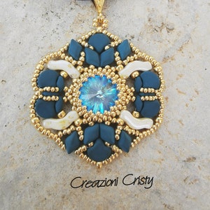 May include: A handmade pendant necklace with a large, iridescent blue crystal at its centre. The pendant is surrounded by teal and white elements, with gold-coloured beads. The necklace has a dark blue cord and a gold-coloured clasp. The text "Creazioni Cristy" is at the bottom.