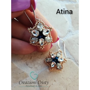 May include: A pair of gold star-shaped earrings with blue and clear crystals. The earrings are handmade in Italy and are called "Atina".
