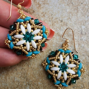 May include: A pair of gold earrings with a square design featuring white, teal and brown beads. The earrings have a floral pattern with a teal crystal in the centre.