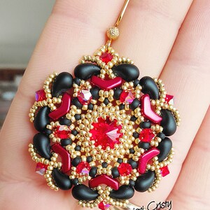 May include: A pair of earrings with a black, red and gold geometric design. The earrings are made with beads and feature a large red crystal in the centre.
