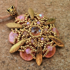 May include: A handmade pendant necklace with a large, decorative, floral-inspired pendant. The pendant features a central crystal, gold beads, pink stones, and gold-coloured accents. It is suspended from a light brown cord.