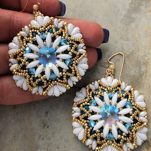 May include: A pair of gold, white, and blue beaded earrings with a crystal center. The earrings are round and have a floral design.