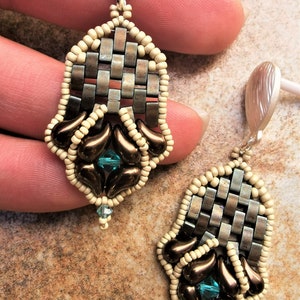 May include: A pair of dangle earrings featuring a woven metal design, brown and cream coloured beads, and a teal gemstone accent.