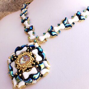 Può includere: Una collana di perline bianche e nere con un ciondolo quadrato che presenta un grande cristallo iridescente al centro. Il ciondolo è circondato da perline più piccole bianche, nere e iridescenti.