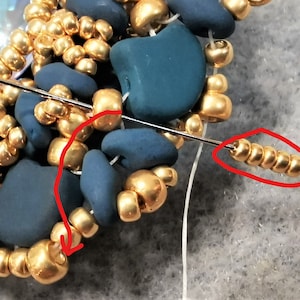 以下が含まれることがあります： 金とターコイズ色のビーズを使ったビーズジュエリープロジェクトのクローズアップ。針は白い糸で糸に通され、金色のビーズの列を通っています。