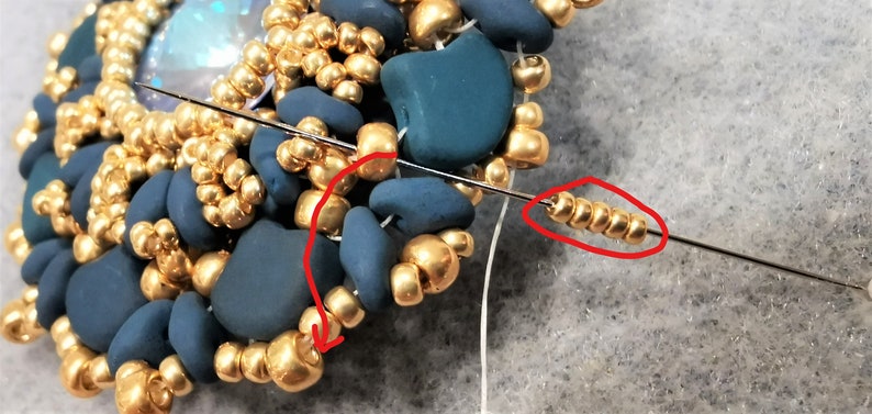以下が含まれることがあります： 金とターコイズ色のビーズを使ったビーズジュエリープロジェクトのクローズアップ。針は白い糸で糸に通され、金色のビーズの列を通っています。