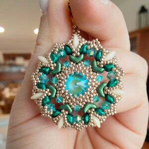 Puede incluir: Un par de pendientes de cuentas verdes y doradas con una piedra preciosa turquesa en el centro. Los pendientes están hechos con cuentas pequeñas y tienen un diseño delicado e intrincado.