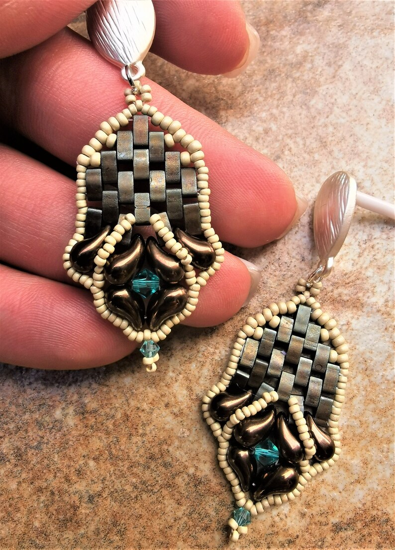 May include: A pair of dangle earrings featuring a woven metal design, brown and cream coloured beads, and teal blue crystals.