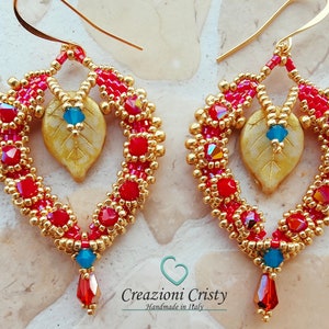 Può includere: Orecchini in perle dorate e rosse con un ciondolo a forma di foglia dorata e una goccia di cristallo rosso. Gli orecchini sono fatti a mano in Italia.