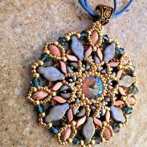 Op de afbeelding: Een gouden, blauwe en koperen kralenketting met een grote, iriserende blauwe kristal in het midden. De hanger heeft de vorm van een bloem met meerdere lagen kralen.