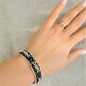 May include: A brown and white beaded bracelet with blue accents. The bracelet is made with small, round beads and has a woven design.
