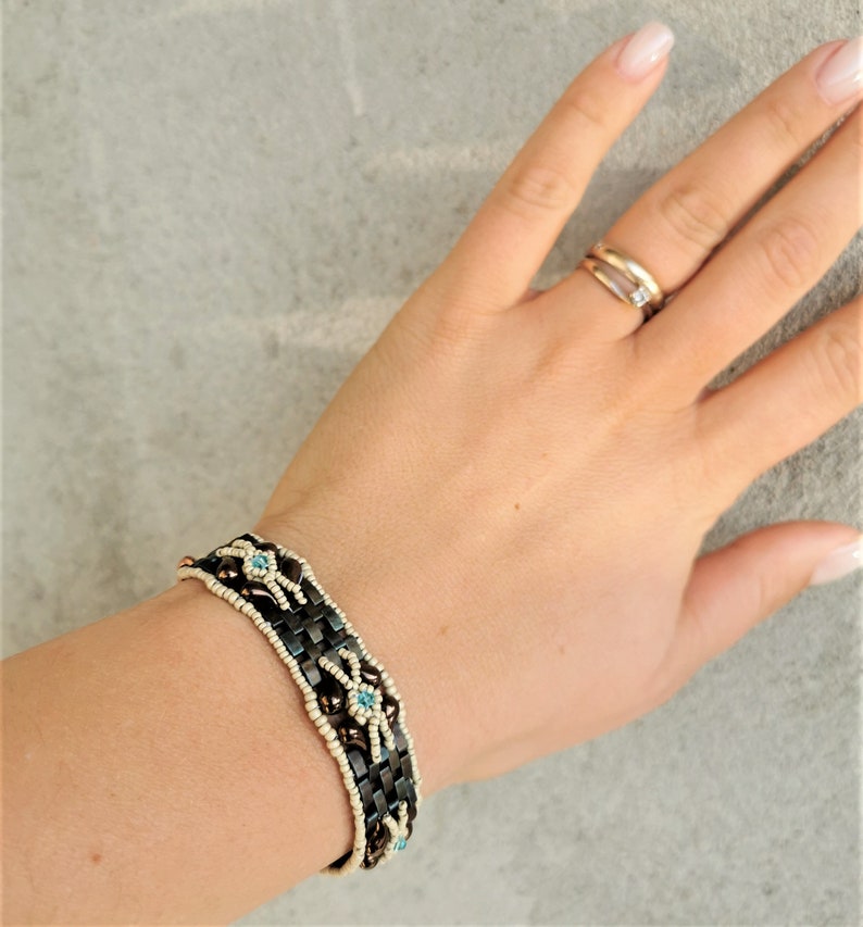 May include: A brown and white beaded bracelet with blue accents. The bracelet is made with small, round beads and has a woven design.