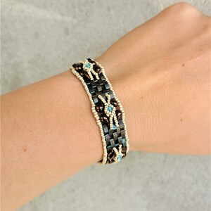 May include: A brown and white beaded bracelet with blue accents. The bracelet is woven with small beads and features a geometric pattern.