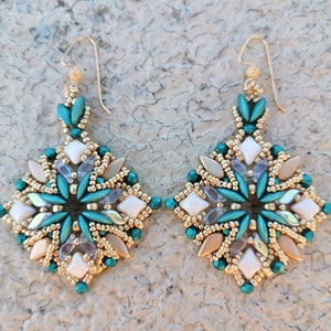Peut inclure: Une paire de boucles d'oreilles en ton or avec un motif géométrique composé de perles turquoise, blanches et dorées.
