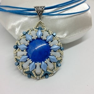 Op de afbeelding: Een blauwe en zilveren kralenketting met een grote blauwe edelsteen in het midden. De hanger is omgeven door kleinere witte en blauwe kralen.