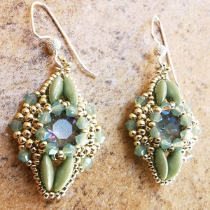Peut inclure: Une paire de boucles d'oreilles pendantes en argent avec un motif géométrique. Les boucles d'oreilles présentent des perles vertes et dorées, et un cristal iridescent transparent au centre.