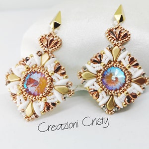 May include: A pair of gold, white, and rose gold beaded earrings with a square design and a iridescent crystal in the center. The earrings are hanging from a gold hook.
