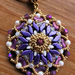 Może przedstawiać: Fioletowy i złoty wisiorek z koralików w kształcie kwiatu. Wisiorek jest wykonany z małych koralików i ma złoty łańcuszek.