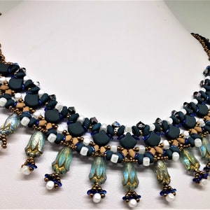 May include: A multi-strand necklace with a cascading design featuring teal, blue, white, and gold beads. The necklace has a geometric pattern and is accented with small, decorative flower-shaped beads.