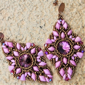 Puede incluir: Un par de pendientes colgantes de color rosa y marrón. Los pendientes están hechos con pequeñas cuentas y presentan un gran cristal rosa facetado en el centro.