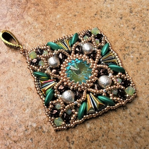 May include: A square pendant with a green, brown, and silver beaded design. A large, clear, faceted crystal is in the center of the pendant.
