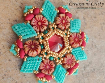 Könnte beinhalten: Eine türkisfarbene und goldene Perlenblume mit einem roten Kristall in der Mitte. Die Blume ist von kleineren roten und weißen Perlen umgeben. Der Text "Creazioni Cristy Handmade in Italy" ist in der oberen rechten Ecke des Bildes zu sehen.