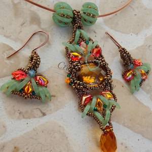 Può includere: Un set di gioielli in perle con una collana con ciondolo e orecchini abbinati. Il ciondolo ha la forma di una lacrima con una grande pietra preziosa color ambra al centro. La collana e gli orecchini sono realizzati con perline di semi marroni, perline di vetro verdi e arancioni e filo di rame.