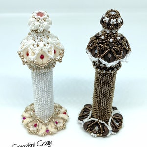 May include: Two decorative beaded bottle stoppers, one white with pink accents and one brown with white accents. The stoppers are shaped like small towers with intricate beadwork.