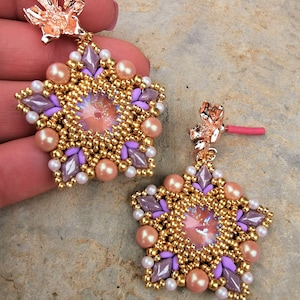 May include: A pair of star-shaped earrings with a gold and purple beaded design. Each earring features a clear iridescent crystal in the center and a rose gold hook.