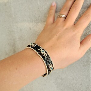 May include: A brown and white beaded bracelet with blue accents. The bracelet is woven with a geometric pattern.