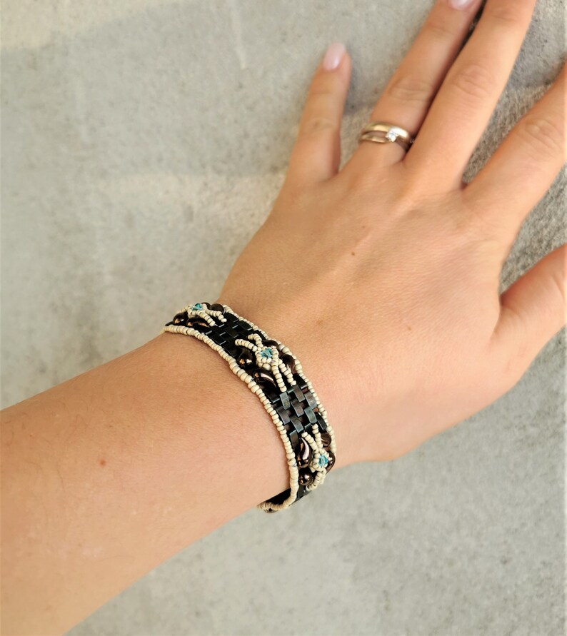 May include: A brown and white beaded bracelet with blue accents. The bracelet is woven with a geometric pattern.