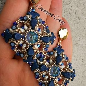 Könnte beinhalten: Ein Paar blaue und goldene Perlenohrringe in Tropfenform. Die Ohrringe haben ein blaues und weißes geometrisches Muster mit einem Kristall in der Mitte.