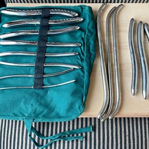 May include: A set of 11 silver medical instruments in a green canvas carrying case. The instruments are curved and have different lengths. The instruments are laid out on a wooden surface.