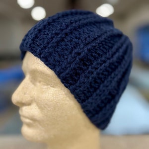 Peut inclure: Un bonnet en tricot bleu marine avec un motif en côtes. Le bonnet est sur une tête de mannequin.