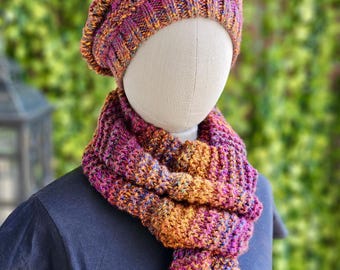 May include: A knitted hat and scarf set in a vibrant mix of colors, including purple, orange, and yellow. The hat is a beret style, and the scarf is thick and textured. The set is displayed on a mannequin, showcasing the cozy and warm design.